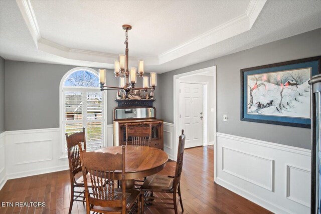 dining room with dark wood-type flooring, a tray ceiling, and an inviting chandelier