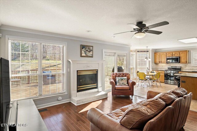 living area featuring ornamental molding, a textured ceiling, hardwood / wood-style flooring, ceiling fan, and a glass covered fireplace