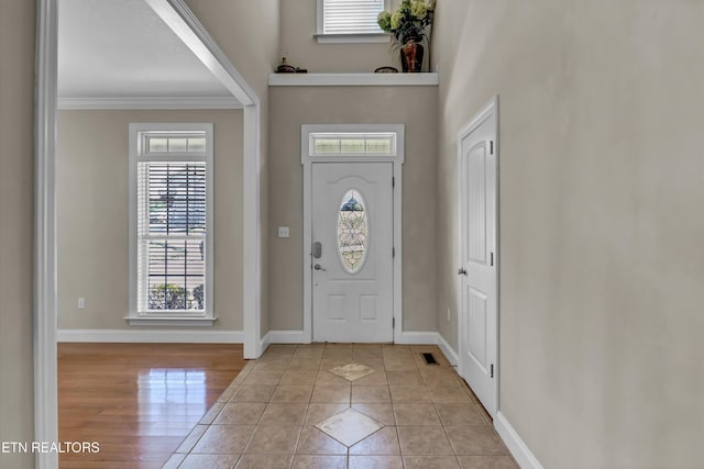 foyer with a high ceiling, light tile patterned floors, crown molding, and baseboards