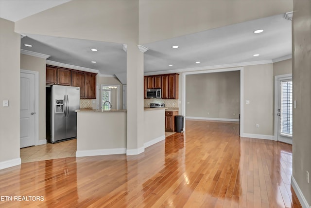 kitchen with light wood-type flooring, ornamental molding, appliances with stainless steel finishes, and a healthy amount of sunlight