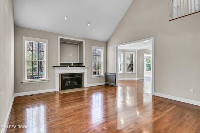 unfurnished living room with a fireplace with flush hearth, high vaulted ceiling, baseboards, and hardwood / wood-style flooring
