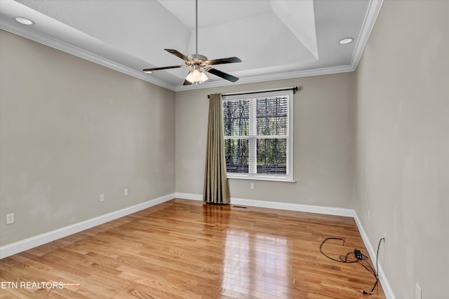 spare room featuring crown molding, baseboards, a raised ceiling, light wood-style floors, and a ceiling fan