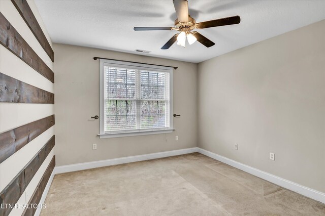 spare room with a tiled fireplace, light carpet, baseboards, and ceiling fan