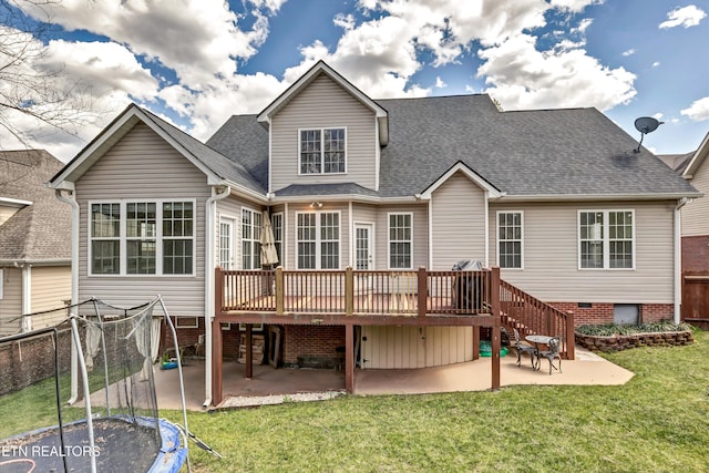 rear view of house with fence, a trampoline, a shingled roof, a yard, and a patio area