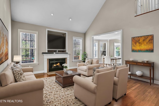 living room with hardwood / wood-style floors, high vaulted ceiling, a fireplace with flush hearth, and baseboards