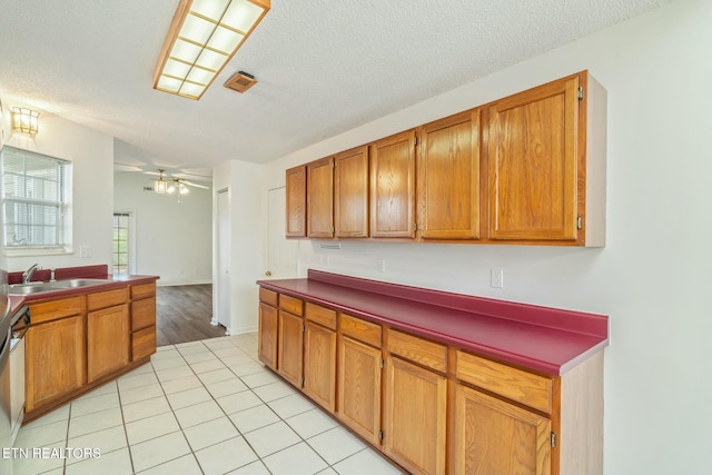 kitchen with light tile patterned floors, a textured ceiling, a sink, visible vents, and brown cabinets