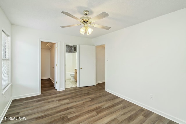 unfurnished bedroom with a walk in closet, baseboards, a ceiling fan, a closet, and wood finished floors