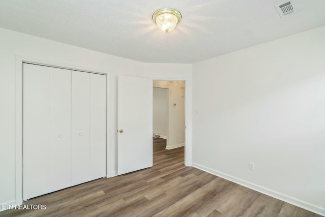 unfurnished bedroom featuring a closet, wood finished floors, a textured ceiling, baseboards, and visible vents