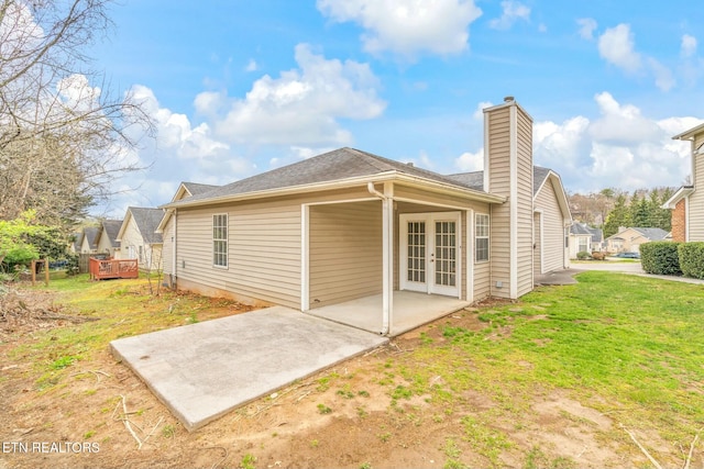 back of property featuring a patio area, french doors, roof with shingles, a chimney, and a yard