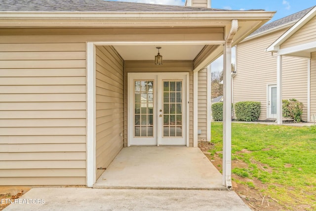 view of exterior entry featuring a lawn, a chimney, a shingled roof, and french doors