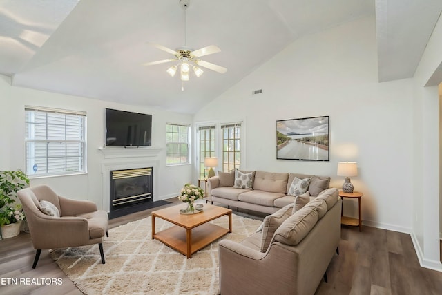 living room with plenty of natural light, a fireplace with flush hearth, wood finished floors, and a ceiling fan