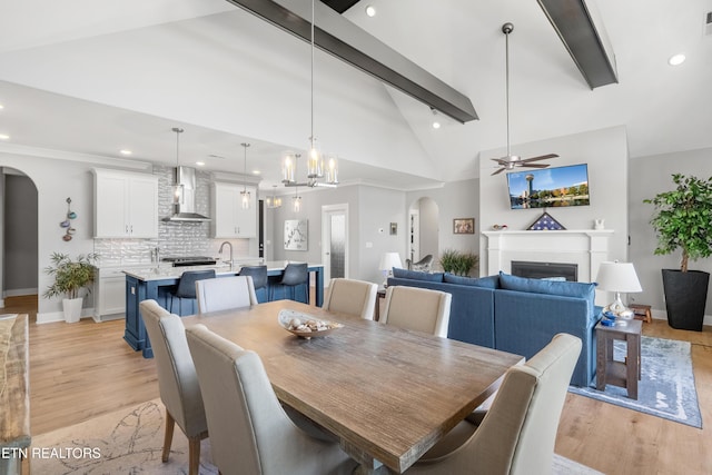 dining area with arched walkways, ceiling fan, light wood-style flooring, and beam ceiling