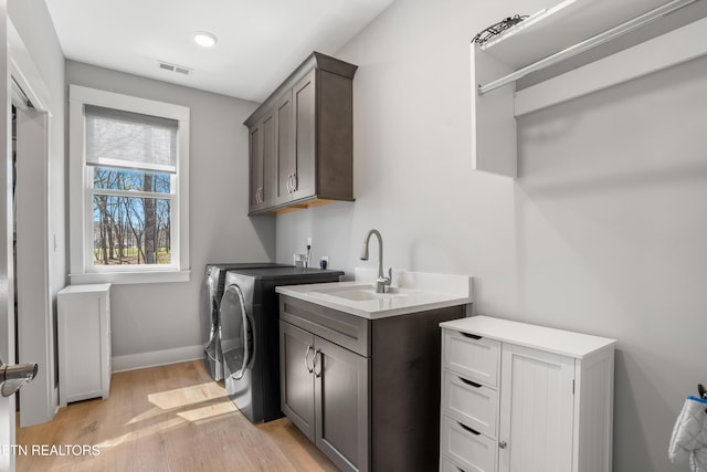 clothes washing area with washer and dryer, light wood-style floors, cabinet space, a sink, and visible vents