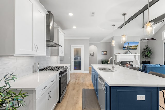 kitchen featuring wall chimney range hood, a sink, black gas stove, blue cabinets, and open floor plan