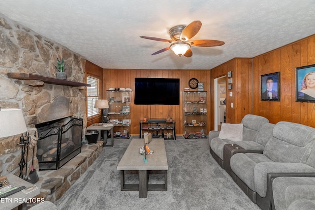 carpeted living room featuring a textured ceiling, a fireplace, wood walls, and a ceiling fan