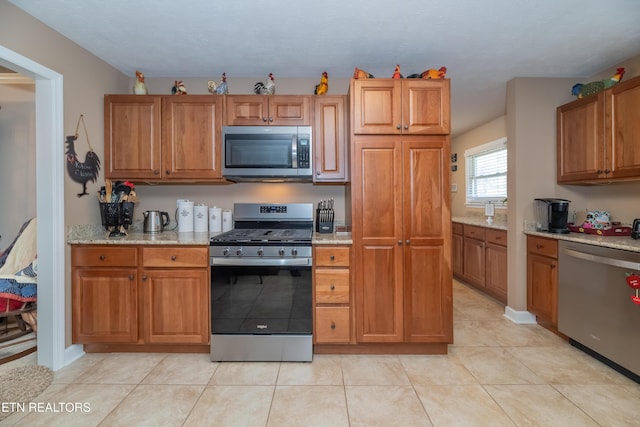 kitchen featuring brown cabinetry, light stone countertops, and appliances with stainless steel finishes