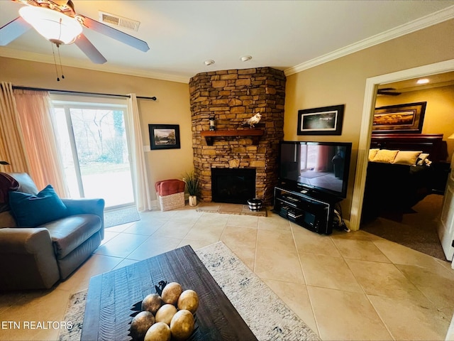 living area with tile patterned flooring, ornamental molding, ceiling fan, visible vents, and a stone fireplace