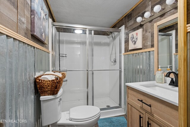 full bathroom featuring a textured ceiling, wooden walls, a shower stall, toilet, and vanity