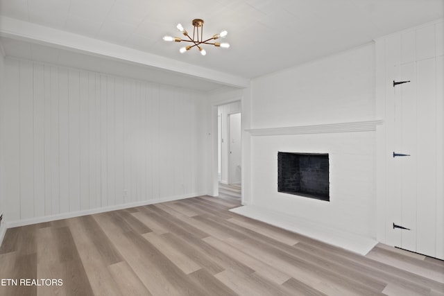 unfurnished living room with baseboards, wood finished floors, a fireplace, and a notable chandelier