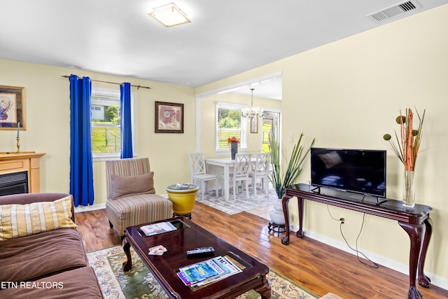 living room with wood finished floors, visible vents, baseboards, a chandelier, and a glass covered fireplace
