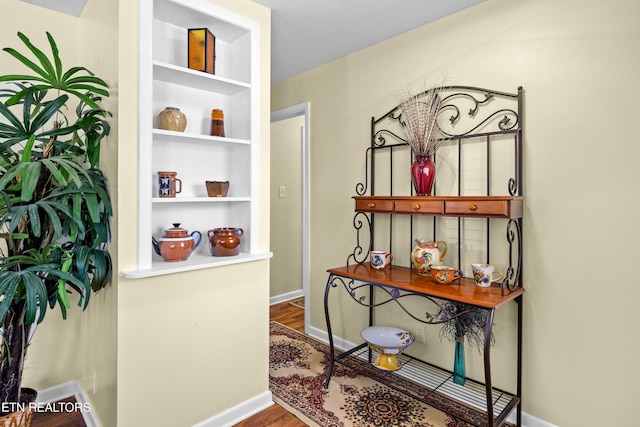 hallway with wood finished floors, built in features, and baseboards