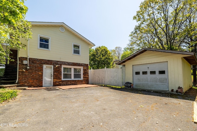 view of property exterior featuring aphalt driveway, fence, an outbuilding, brick siding, and stairs