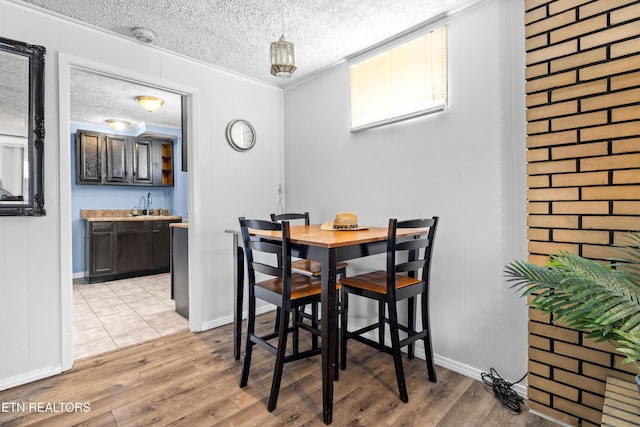 dining area featuring wet bar, a textured ceiling, light wood finished floors, and baseboards