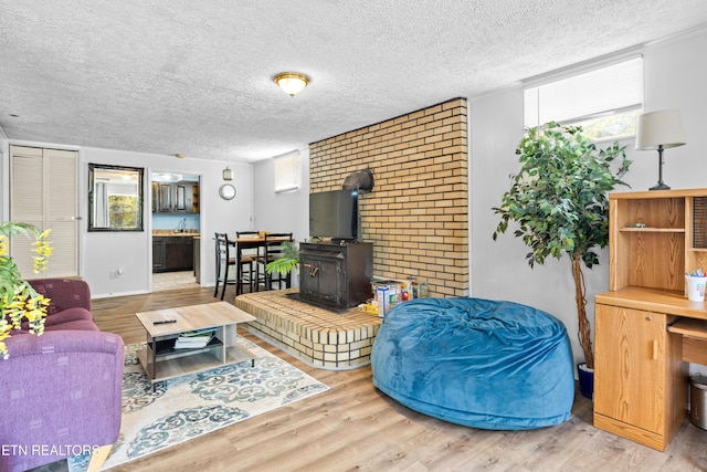 living room with wood finished floors, a textured ceiling, a wood stove, and a healthy amount of sunlight