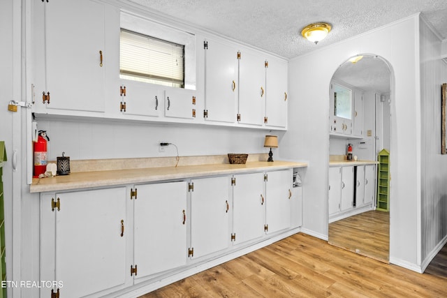 kitchen featuring light countertops, arched walkways, light wood-style floors, a textured ceiling, and white cabinetry