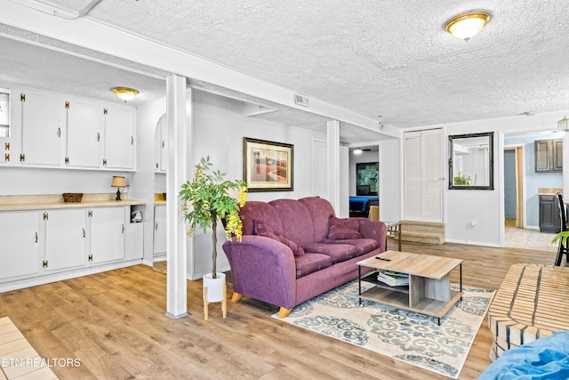 living room with visible vents, light wood-style flooring, baseboards, and a textured ceiling