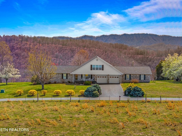 view of front facade with concrete driveway, an attached garage, a wooded view, a front yard, and a mountain view