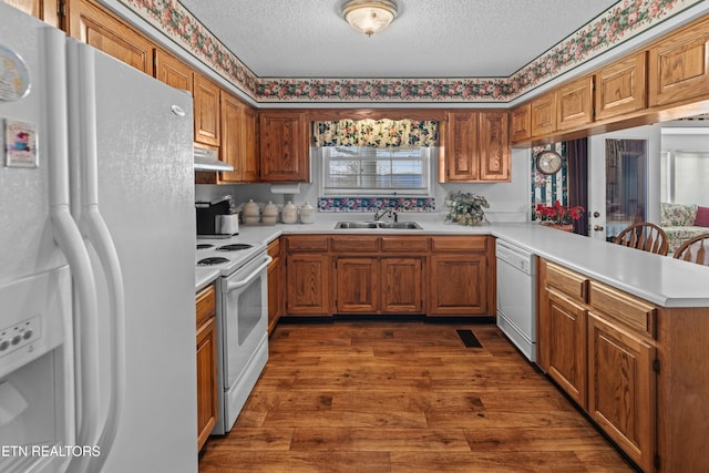 kitchen with light countertops, a peninsula, white appliances, under cabinet range hood, and a sink