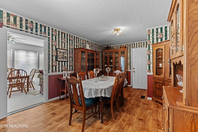 dining room with light wood-type flooring, wallpapered walls, baseboards, and a textured ceiling