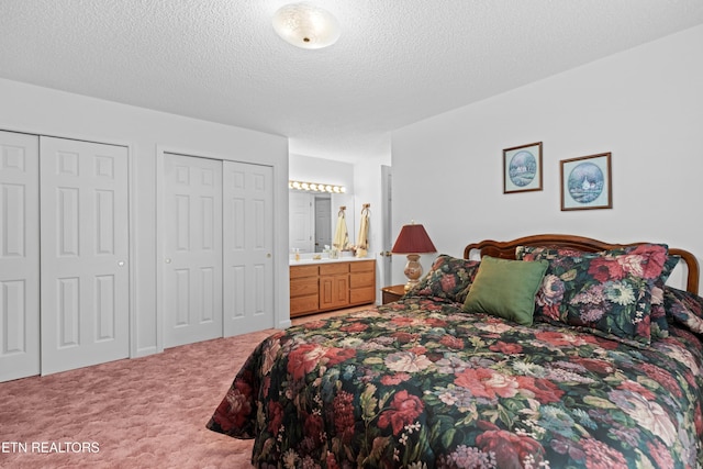 carpeted bedroom featuring ensuite bathroom, a textured ceiling, and two closets