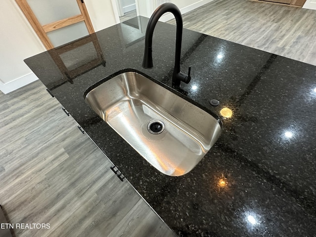 interior details featuring a sink, dark stone counters, and wood finished floors