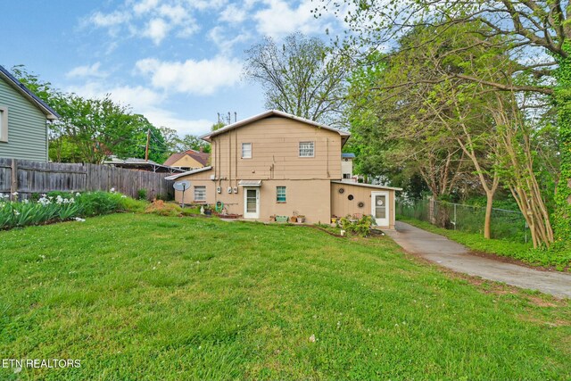 rear view of house featuring concrete driveway, fence, and a yard