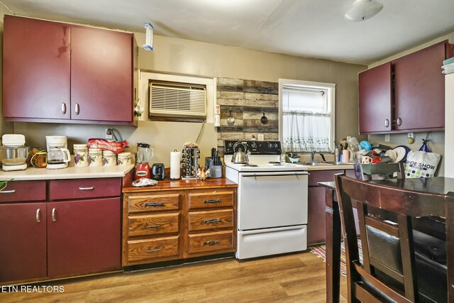 kitchen featuring a wall mounted air conditioner, a sink, red cabinets, light wood-style flooring, and electric range