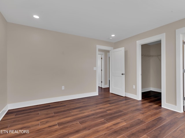 unfurnished bedroom with baseboards, dark wood-style flooring, recessed lighting, and a walk in closet