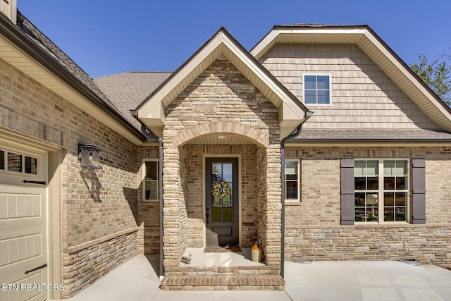 property entrance featuring stone siding, a garage, and roof with shingles