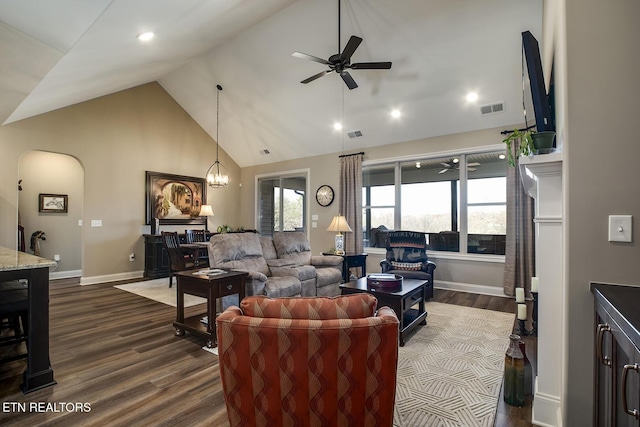 living area with high vaulted ceiling, dark wood-type flooring, arched walkways, ceiling fan, and visible vents