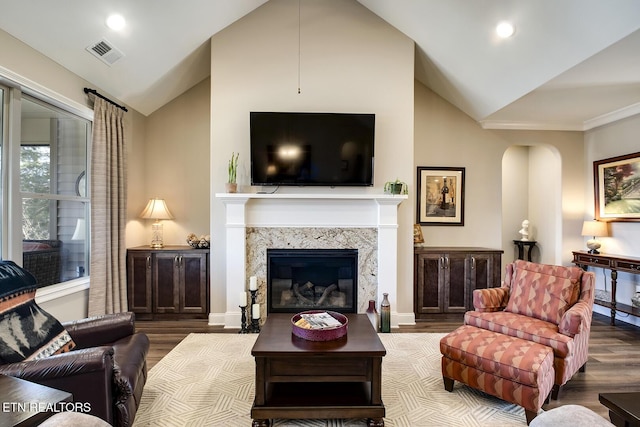 living area featuring visible vents, a high end fireplace, wood finished floors, arched walkways, and lofted ceiling