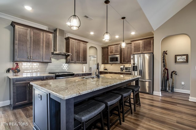kitchen with a sink, stainless steel appliances, wall chimney range hood, arched walkways, and decorative backsplash