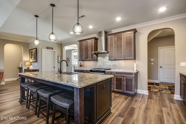kitchen with gas range, wall chimney exhaust hood, arched walkways, and a sink