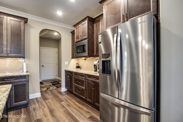 kitchen with stainless steel appliances, dark brown cabinets, arched walkways, light stone counters, and dark wood-style floors