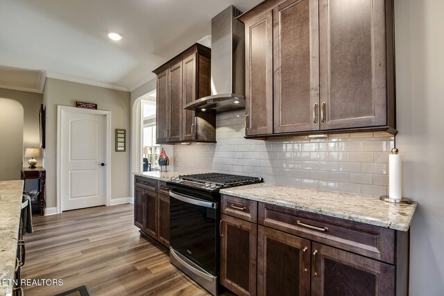 kitchen with stainless steel range with gas stovetop, decorative backsplash, arched walkways, wall chimney range hood, and dark brown cabinetry
