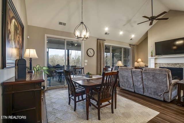 dining room featuring a fireplace, ceiling fan with notable chandelier, dark wood-type flooring, and visible vents