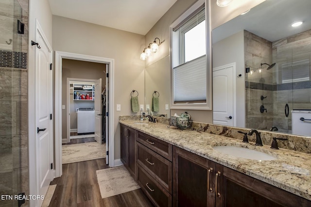 bathroom featuring a spacious closet, a shower stall, a sink, washer / clothes dryer, and wood finished floors