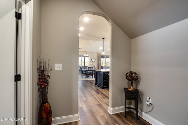 hall with baseboards, arched walkways, and wood finished floors