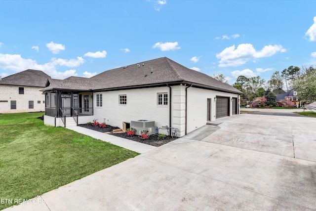 back of property featuring concrete driveway, central air condition unit, a garage, a yard, and a sunroom