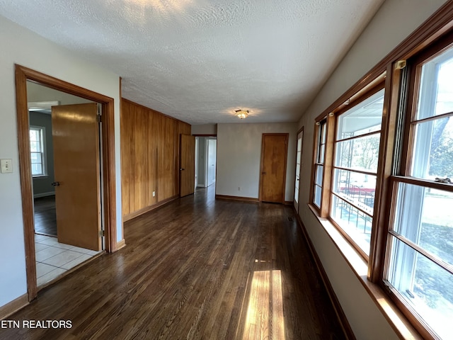 unfurnished room featuring baseboards, dark wood-type flooring, a healthy amount of sunlight, and a textured ceiling